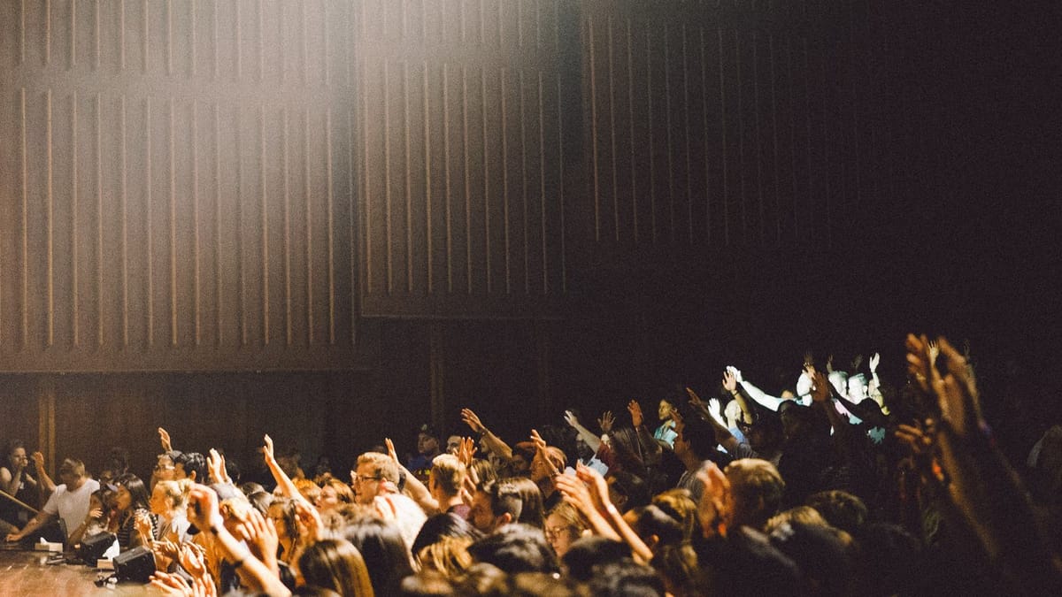 An audience in a darkened hall with hands raised toward the stage