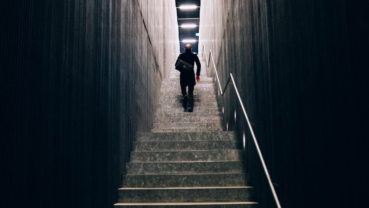 A lone figure walking up a dimly lit concrete stairwell