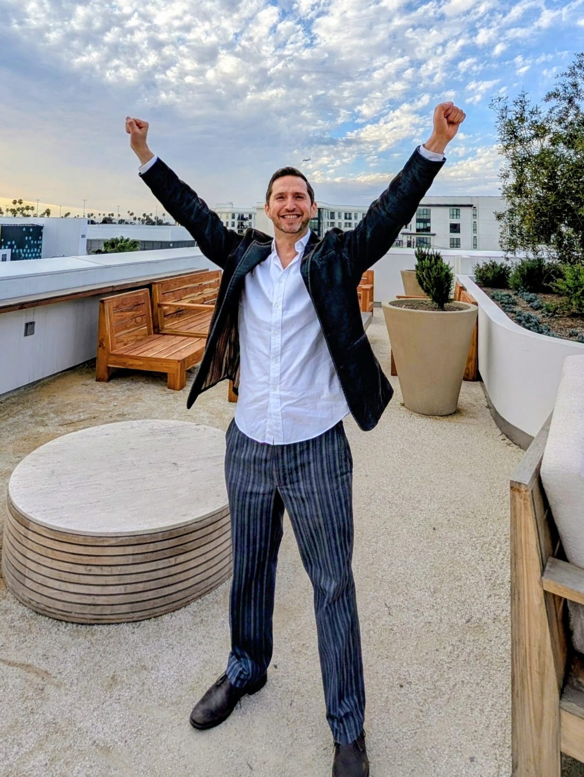 Noel on a rooftop terrace in Los Angeles, both fists in the air, grinning